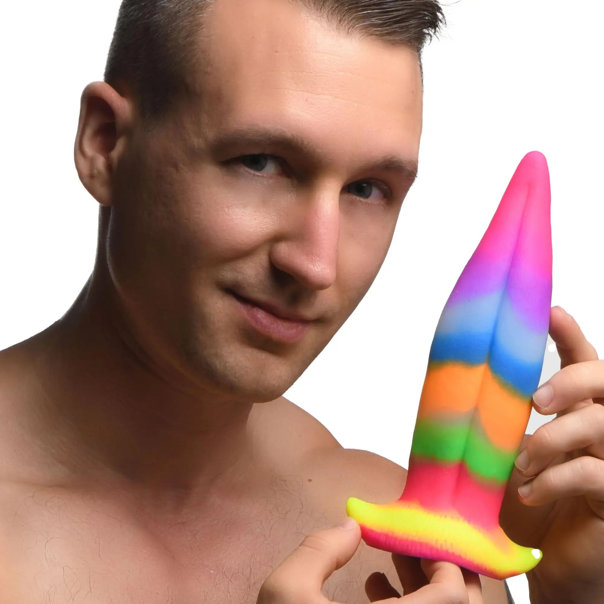 A man holds a rainbow-colored, glow-in-the-dark Creature Cocks Unicorn Kiss silicone dildo against a white background.