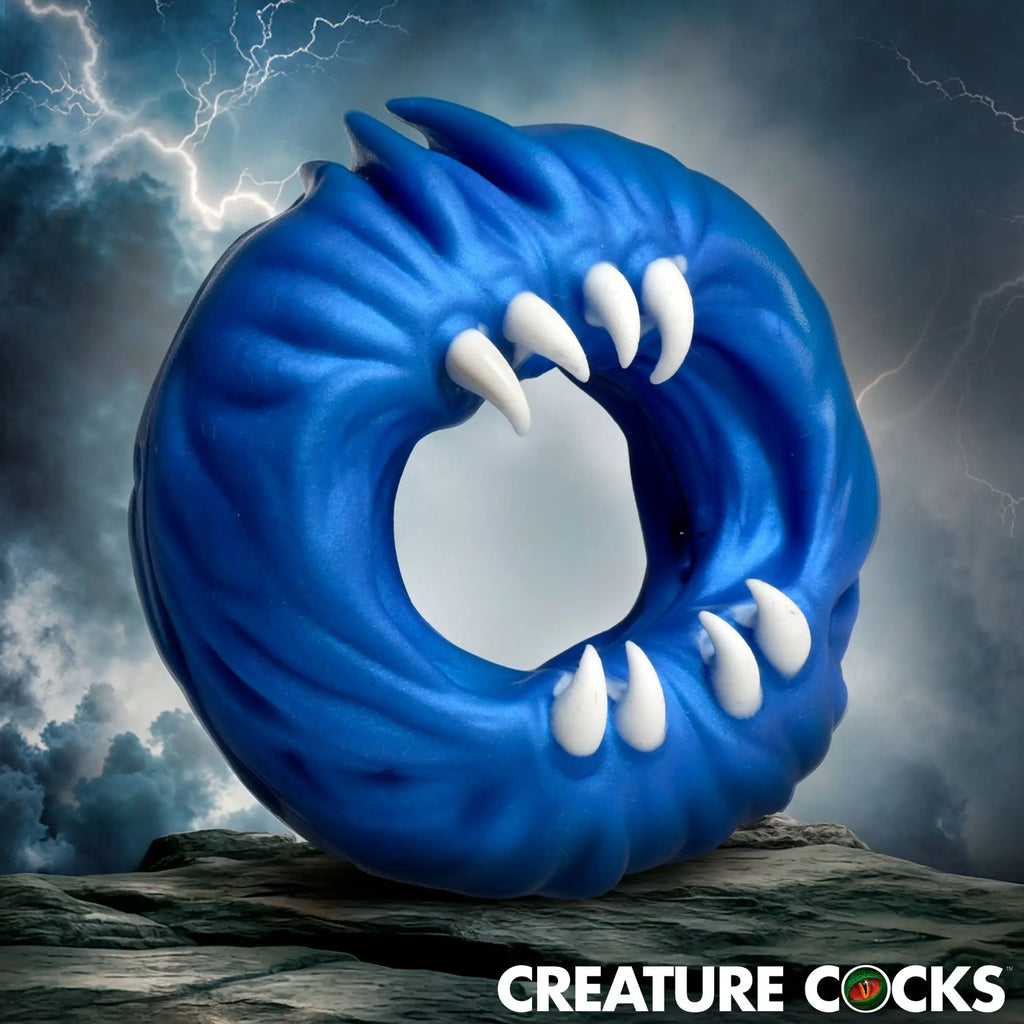 Creature Cocks Venom Loop blue silicone cock ring with textured details and white monster teeth against a stormy backdrop.
