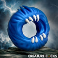 Creature Cocks Venom Loop blue silicone cock ring with textured details and white monster teeth against a stormy backdrop.