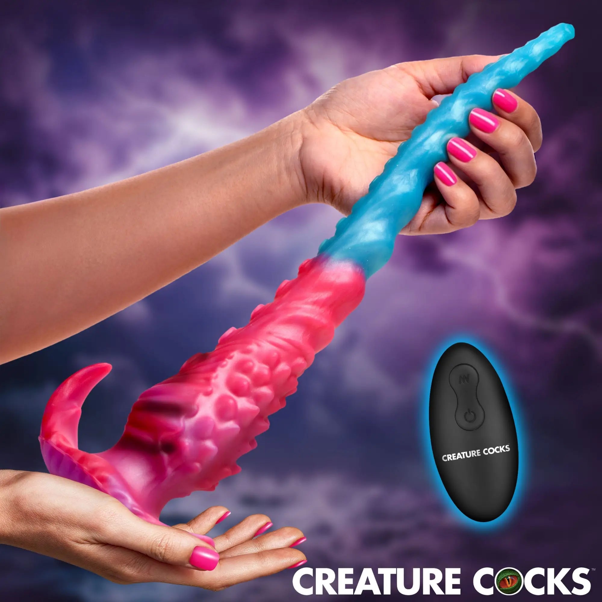 Hands holding a Creature Cocks Vibropus: a textured, pink-to-blue gradient silicone dildo with a remote controller.