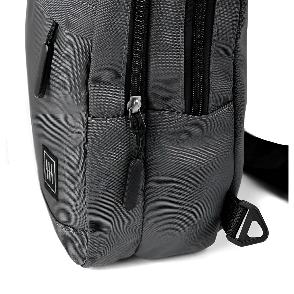Dark gray canvas crossbody sling bag with black zippers and small square logo patch for everyday use
