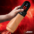 Hand holding a black and tan JOCK Advanced Mega Suck masturbator with digital display against a red, fiery background.