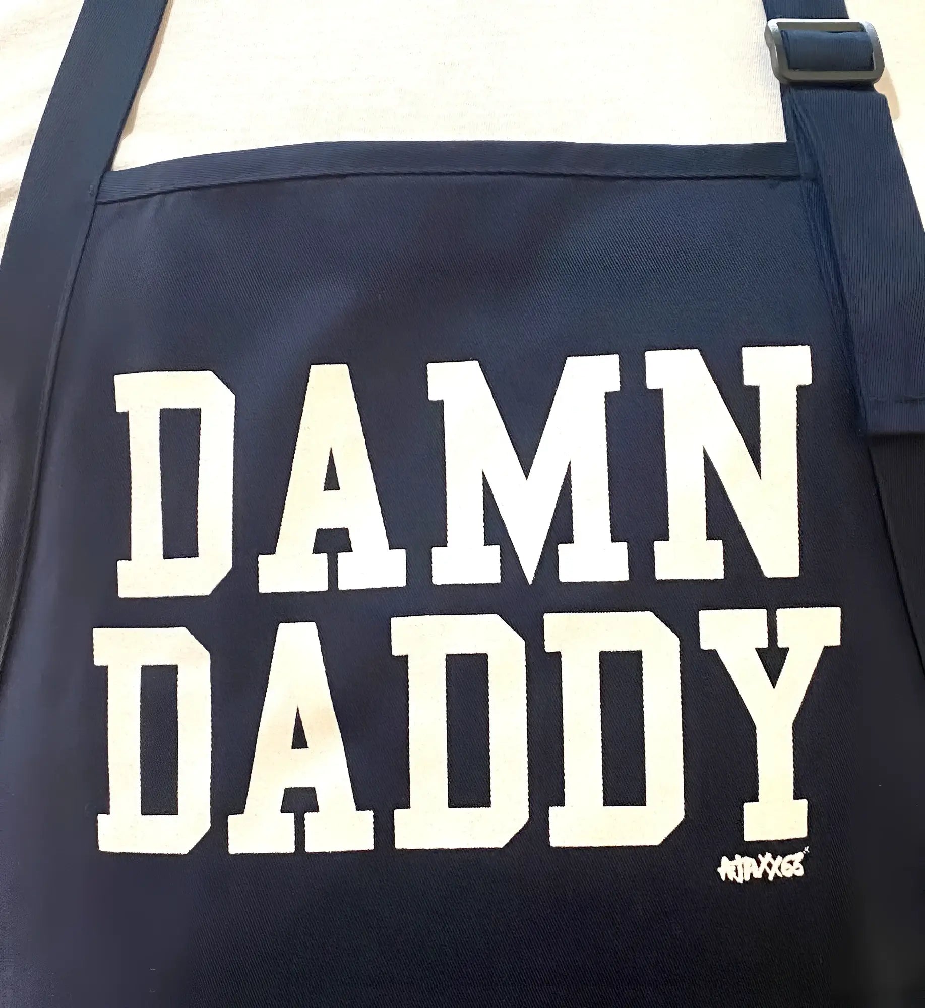 Navy blue canvas shoulder bag with bold white damn daddy lettering and small graffiti style signature in the corner