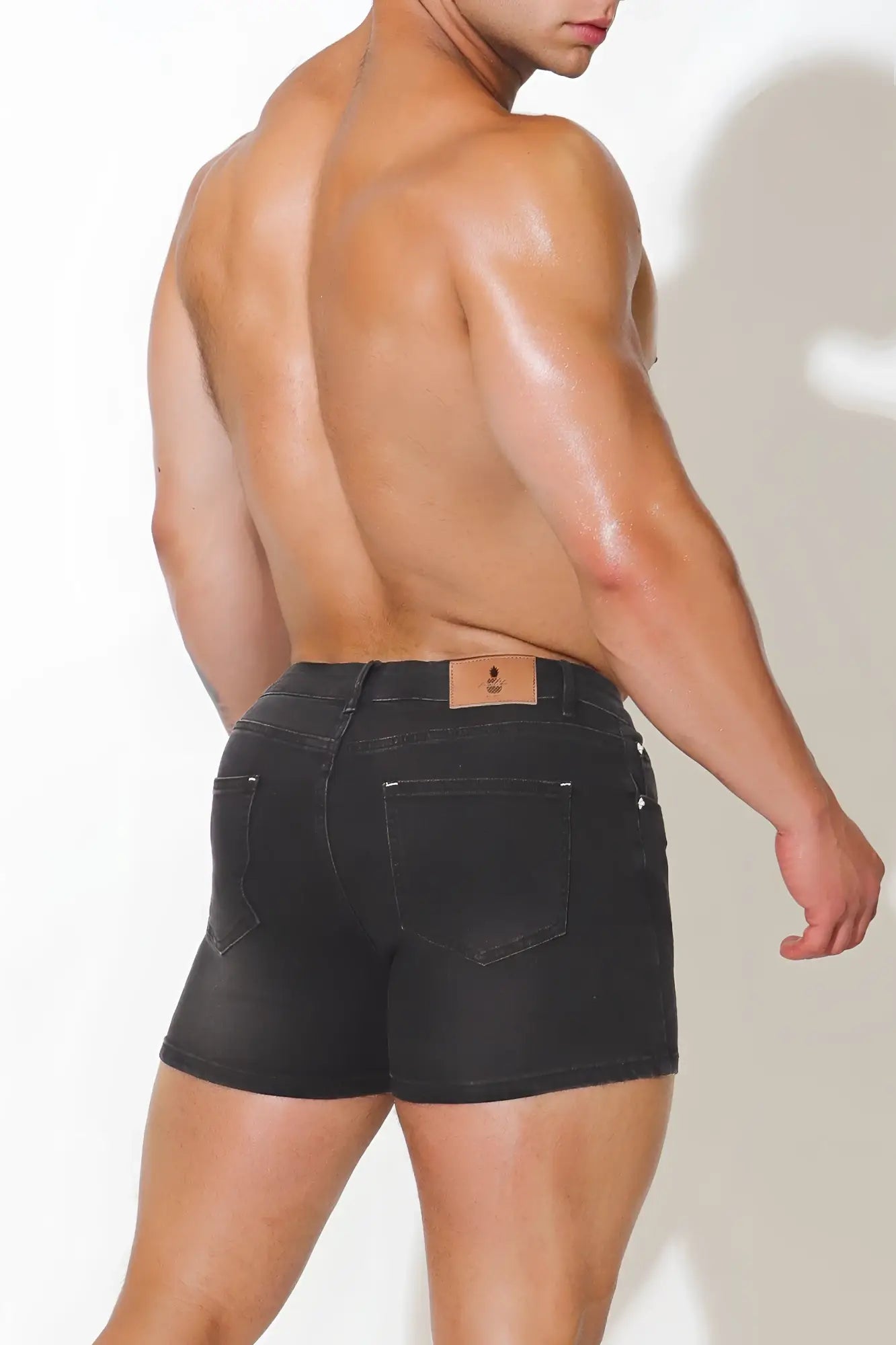 Black denim in-your-dreams 3.5 inch short shorts with a brown leather brand patch on the waistband back view