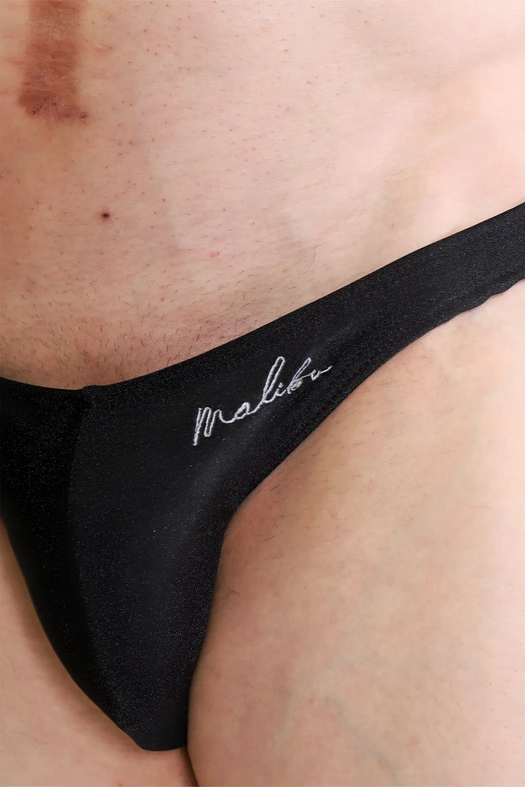 Black malibu dynamic classic scrunch-butt brief thong in jet black with white cursive embroidery showing the back side