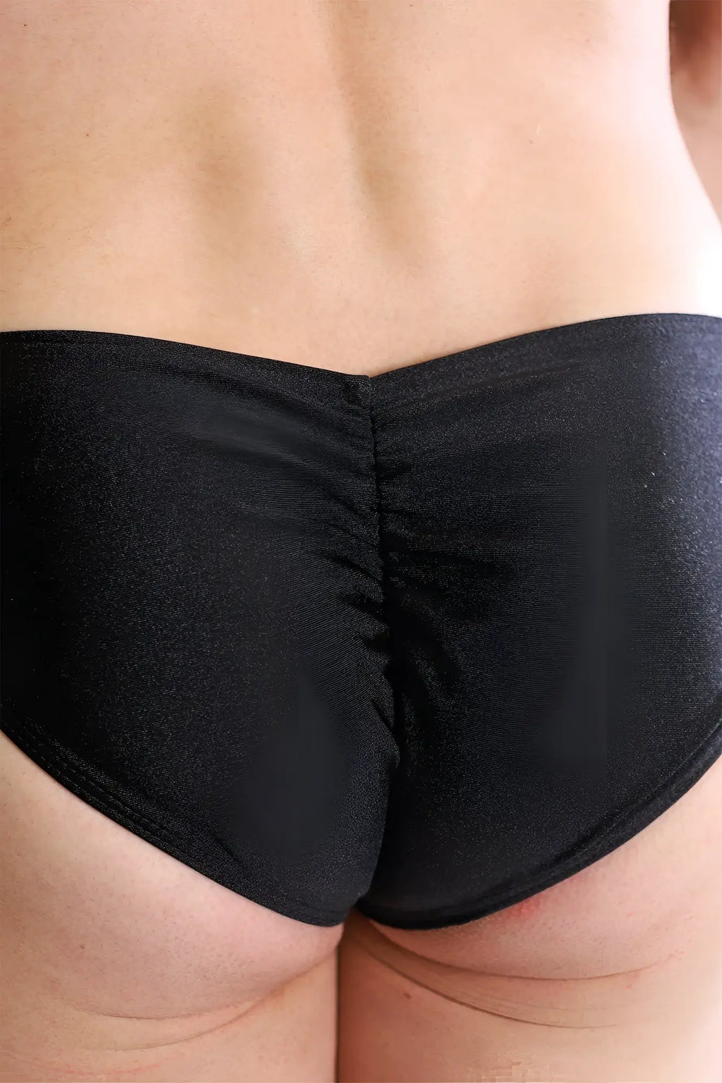 Black shiny stretchy fabric briefs with ruched back design shown from the back in dynamic classic scrunch-butt brief