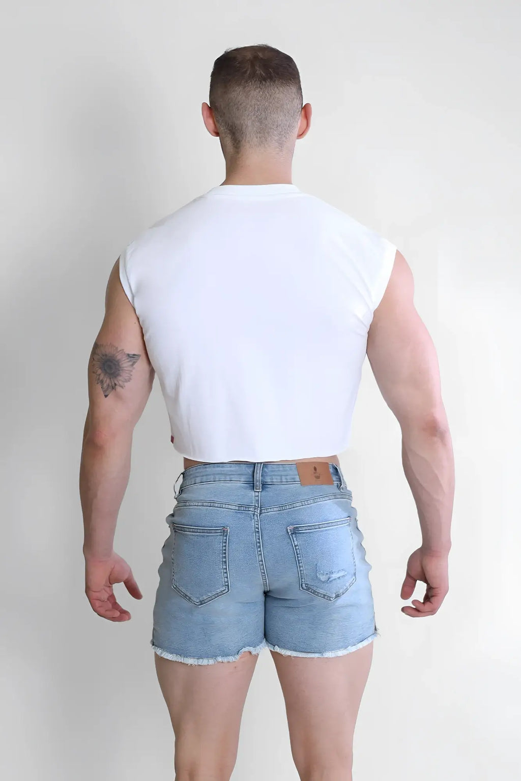 Light-wash denim shorts with frayed hem and classic back pockets shown from the back paired with escapism muscle-fit crop