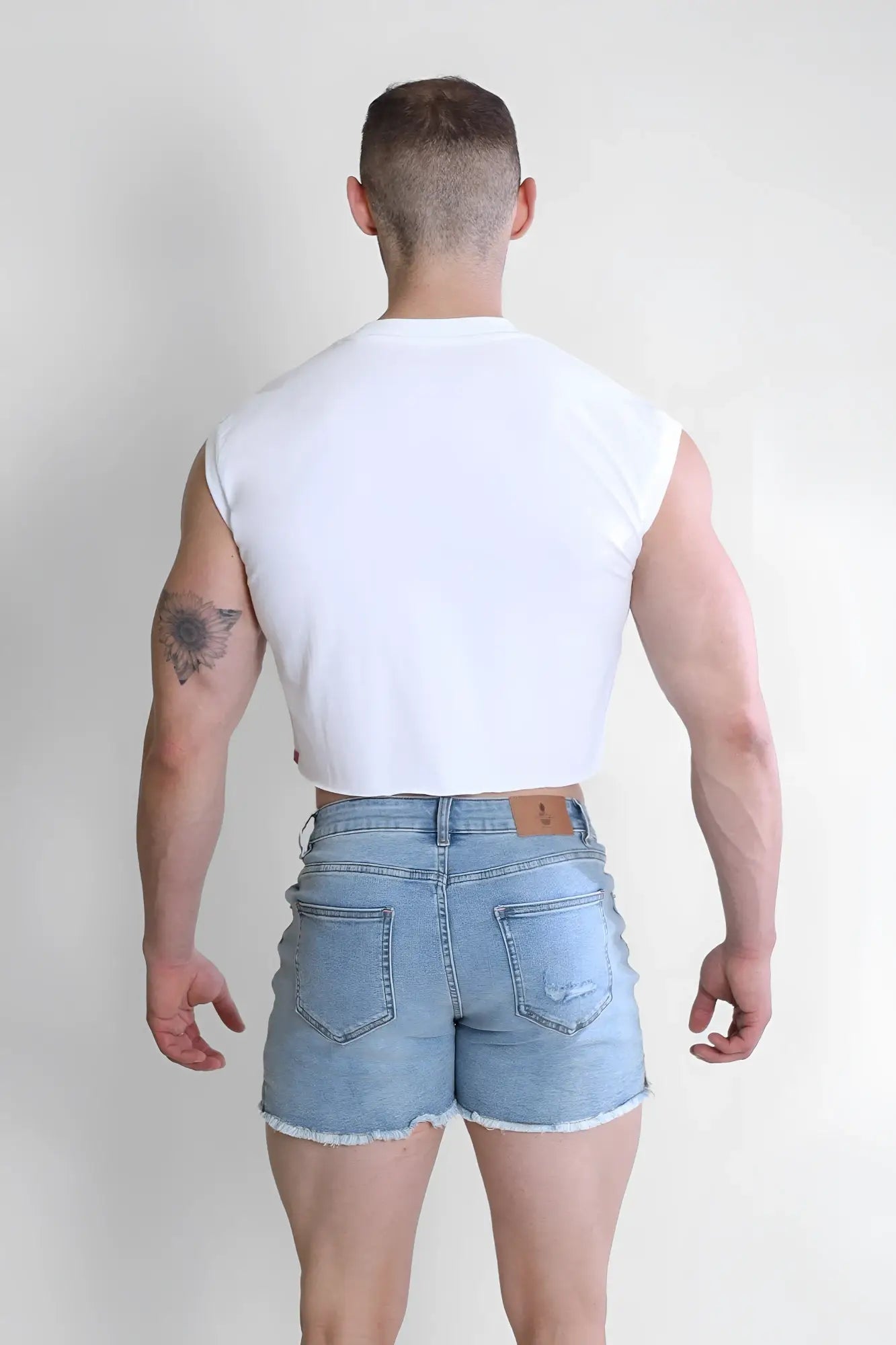Light-wash denim shorts with frayed hem and classic back pockets shown from the back paired with escapism muscle-fit crop