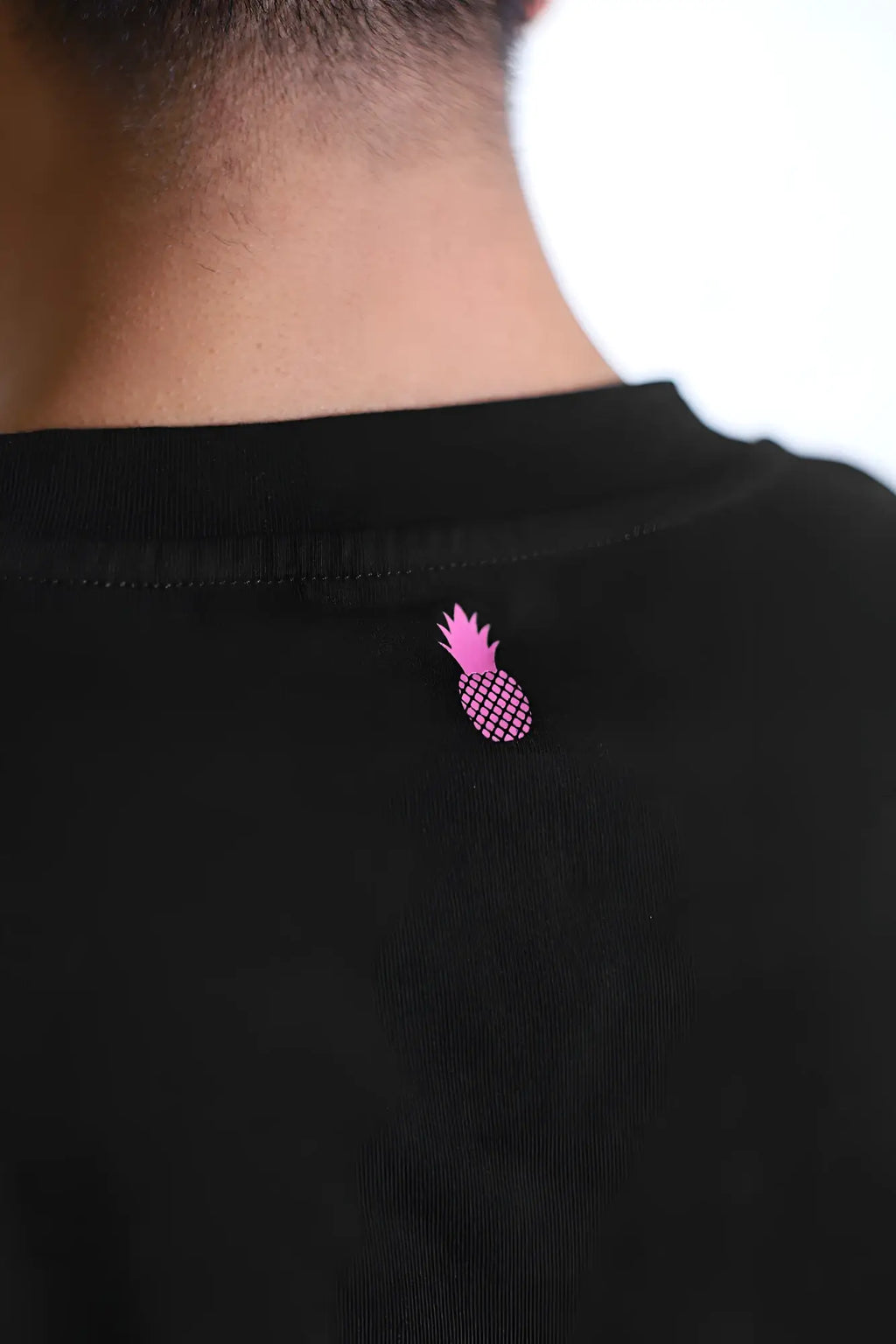 The back of a black escapism muscle-fit crop tank features a small pink pineapple graphic for a bold look