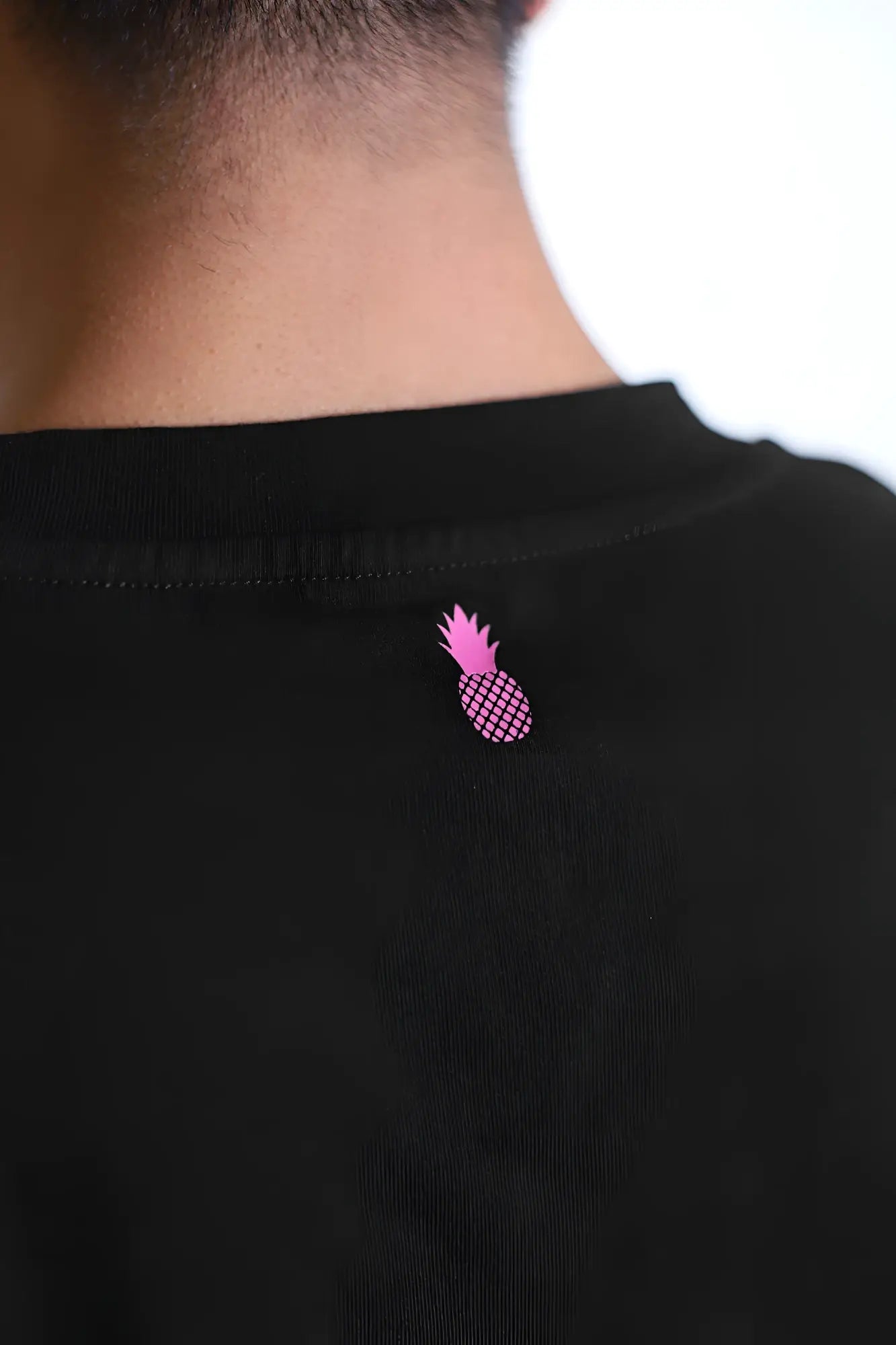 The back of a black escapism muscle-fit crop tank features a small pink pineapple graphic for a bold look
