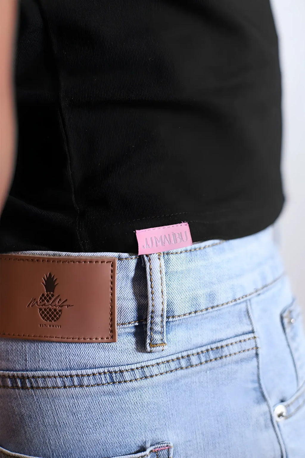 Light blue denim jeans with brown leather patch embroidered pineapple logo and pink fabric tag showing back side