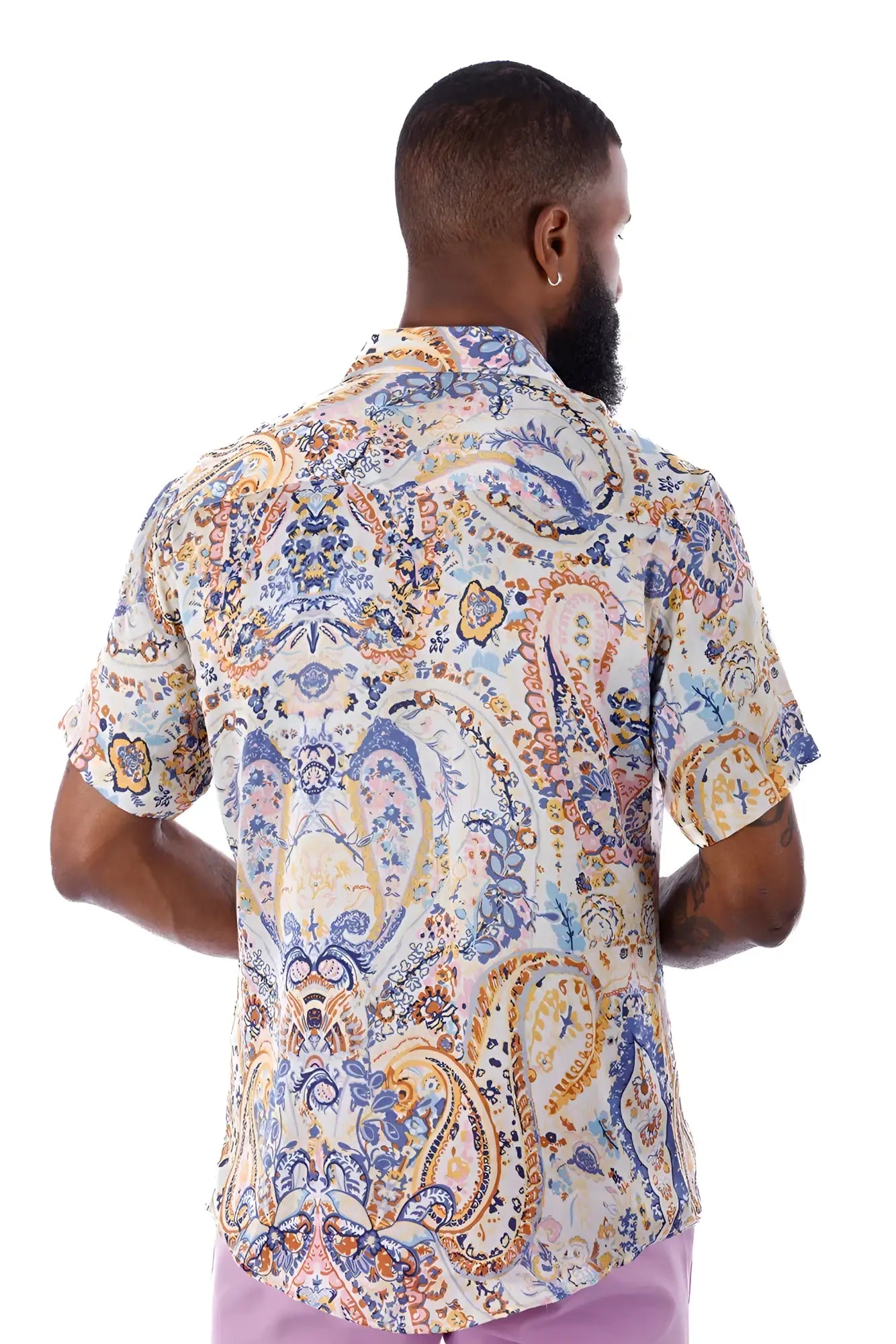 A man wearing an exclusive buzz s s shirt with intricate blue gold and cream paisley pattern on a light background