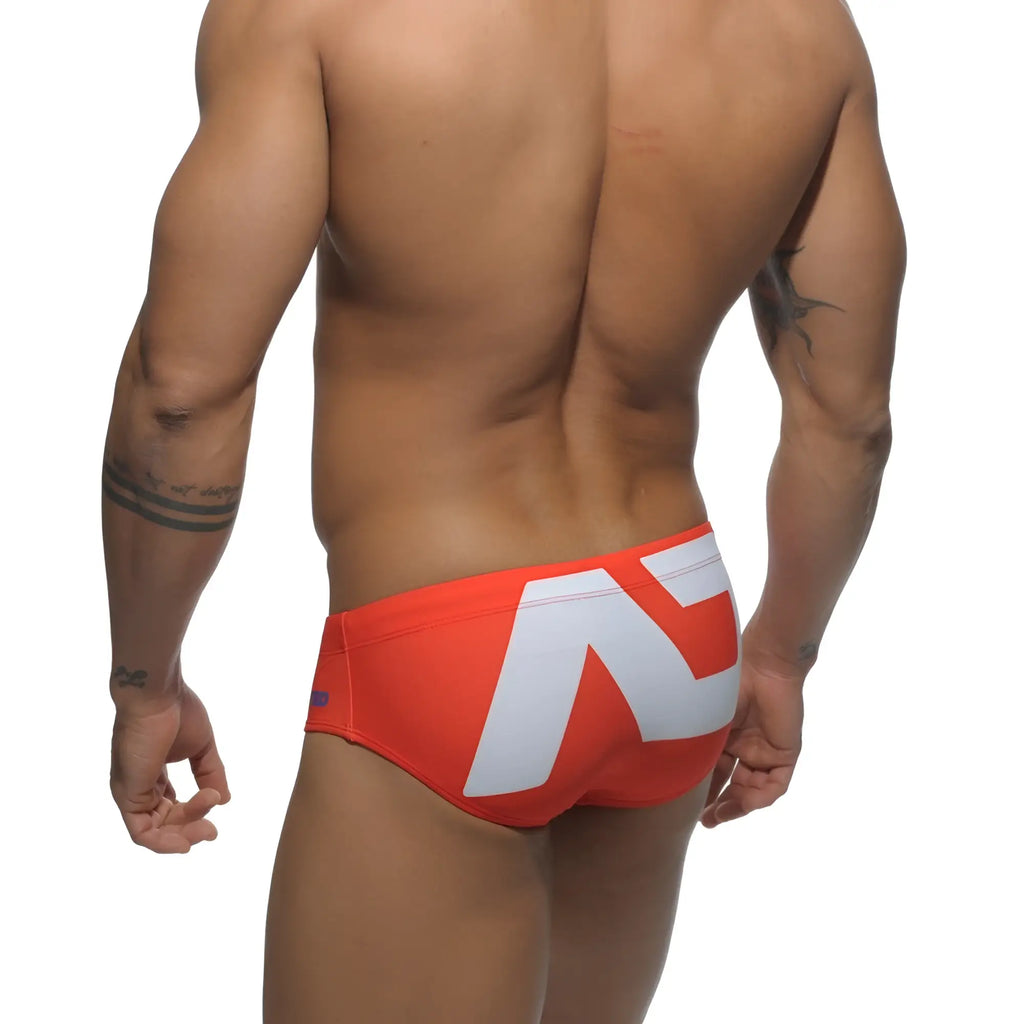 Extra-large logo brief vibrant orange swim trunks with bold white geometric logo on the back side