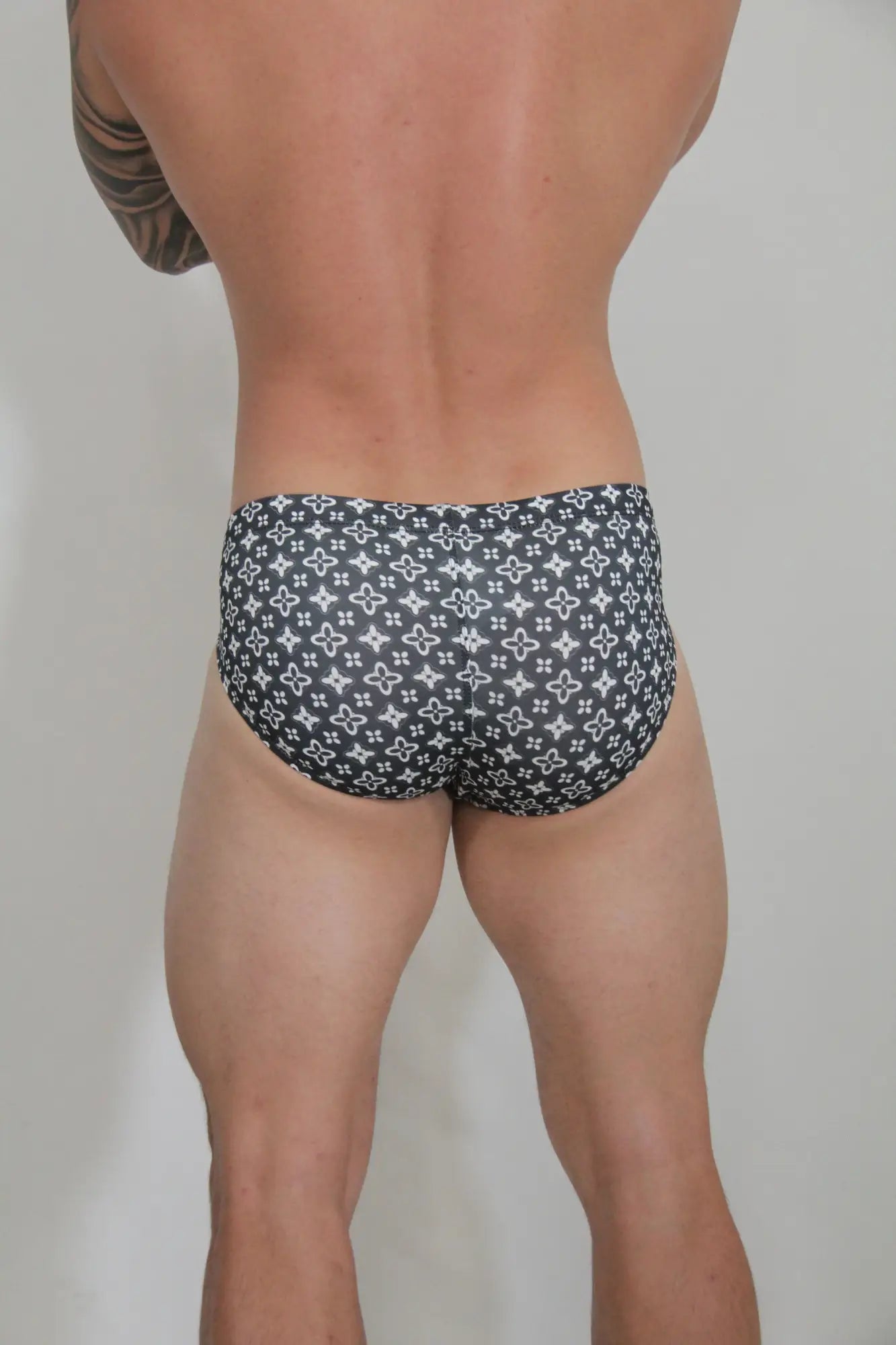 Black fancy symbols swim brief with repeating white monogram pattern on briefs front side