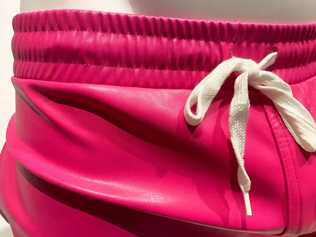 Bright pink faux leather shorts with a white drawstring waistband in a stylish faux leather short design
