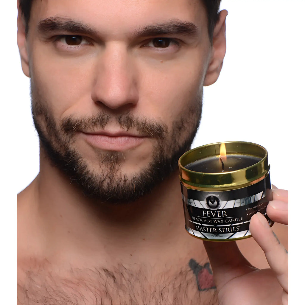 Gold-rimmed tin holding a black hot wax candle with lit wick labeled fever from the master series