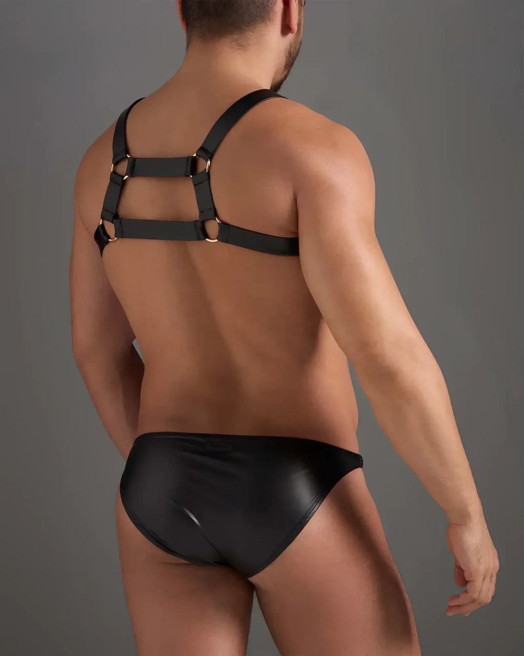 Black leather flex harness with gold metal rings worn over matching black patent leather brief front view