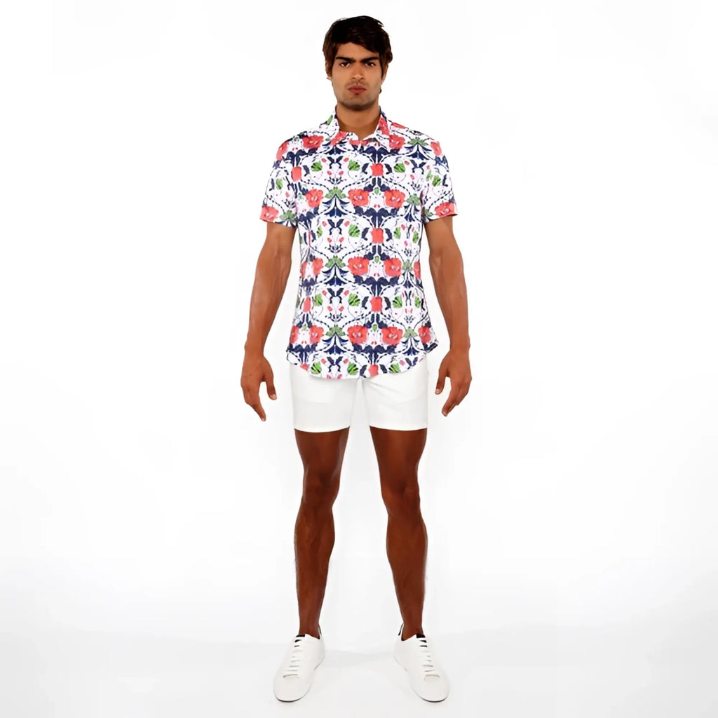 A man wearing a floral print stretch knit shirt with vibrant red blue and green flowers on a white background