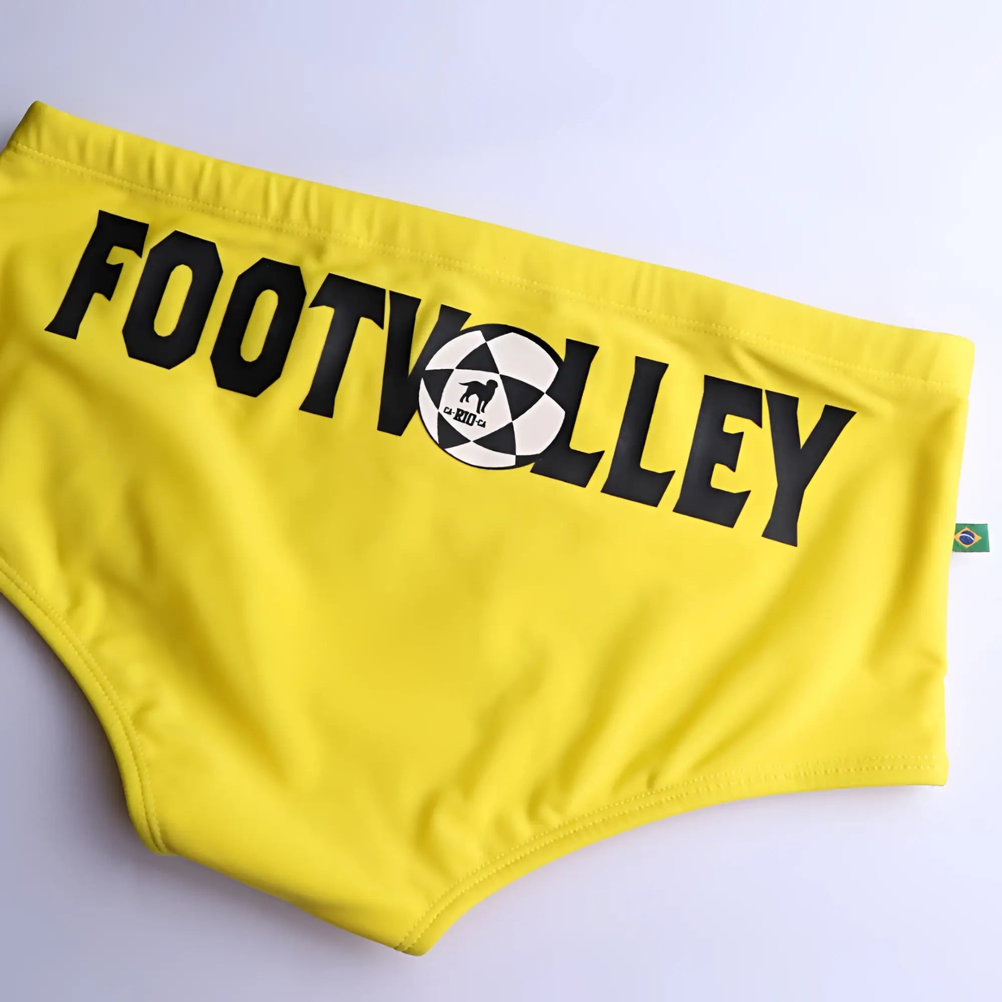 Bright yellow men’s swim trunks with bold black footvolley lettering and a soccer ball graphic in a traditional cut