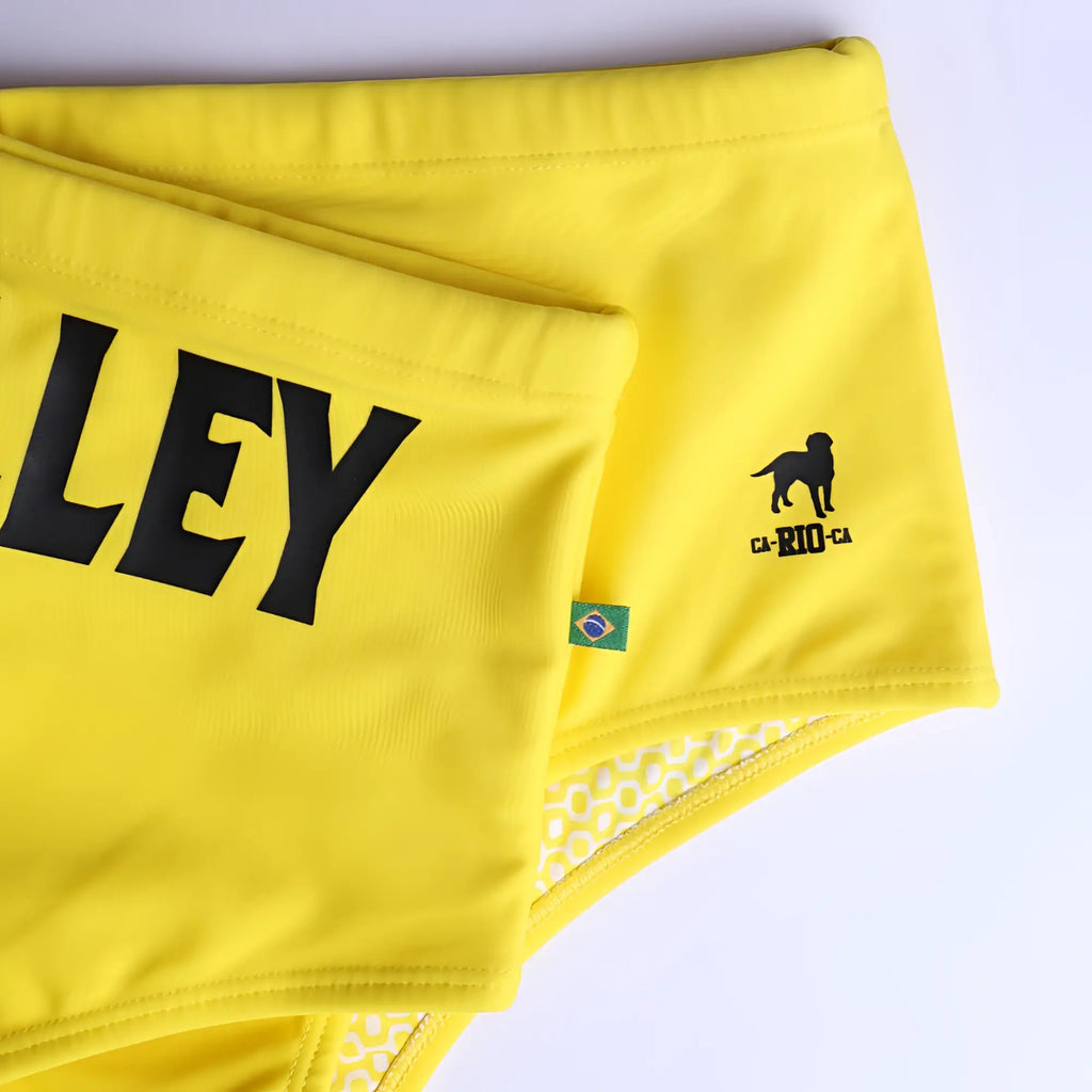 Bright yellow men’s designer footvolley sunga swim trunks with bold black ley lettering and Brazilian flag patch