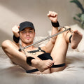 Frisky The Bondage Bar: A man in a cap and black harness uses a silver spreader bar with black padded wrist cuffs.