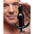A hand holds a black, bumpy Frisky Vibrating Anal Plug with a T-bar base, shown with motion lines indicating vibration.