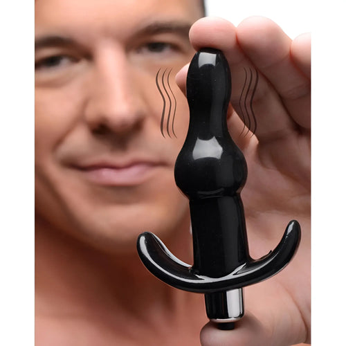 A hand holds a black, bumpy Frisky Vibrating Anal Plug with a T-bar base, shown with motion lines indicating vibration.