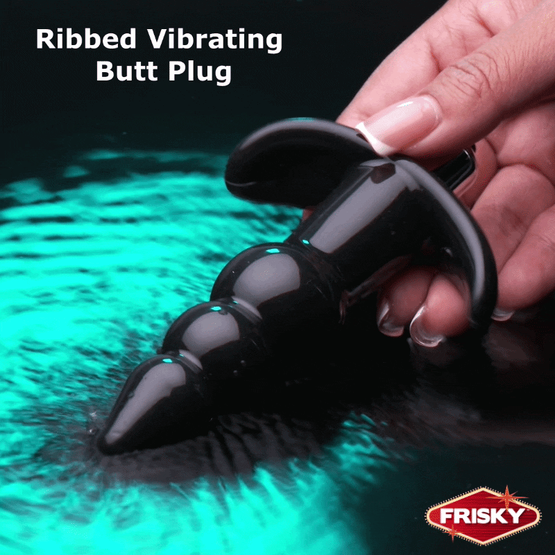 A hand holds a shiny, black Frisky Ribbed Vibrating Butt Plug above a surface with vibrant turquoise water ripples.