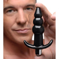 A hand holds a sleek, black Frisky Ribbed Vibrating Butt Plug with a T-bar base, depicted with motion lines.