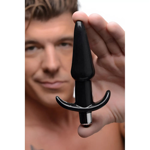 A man holds a smooth, glossy black Frisky Smooth Vibrating Anal Plug with a flared base against a white background.