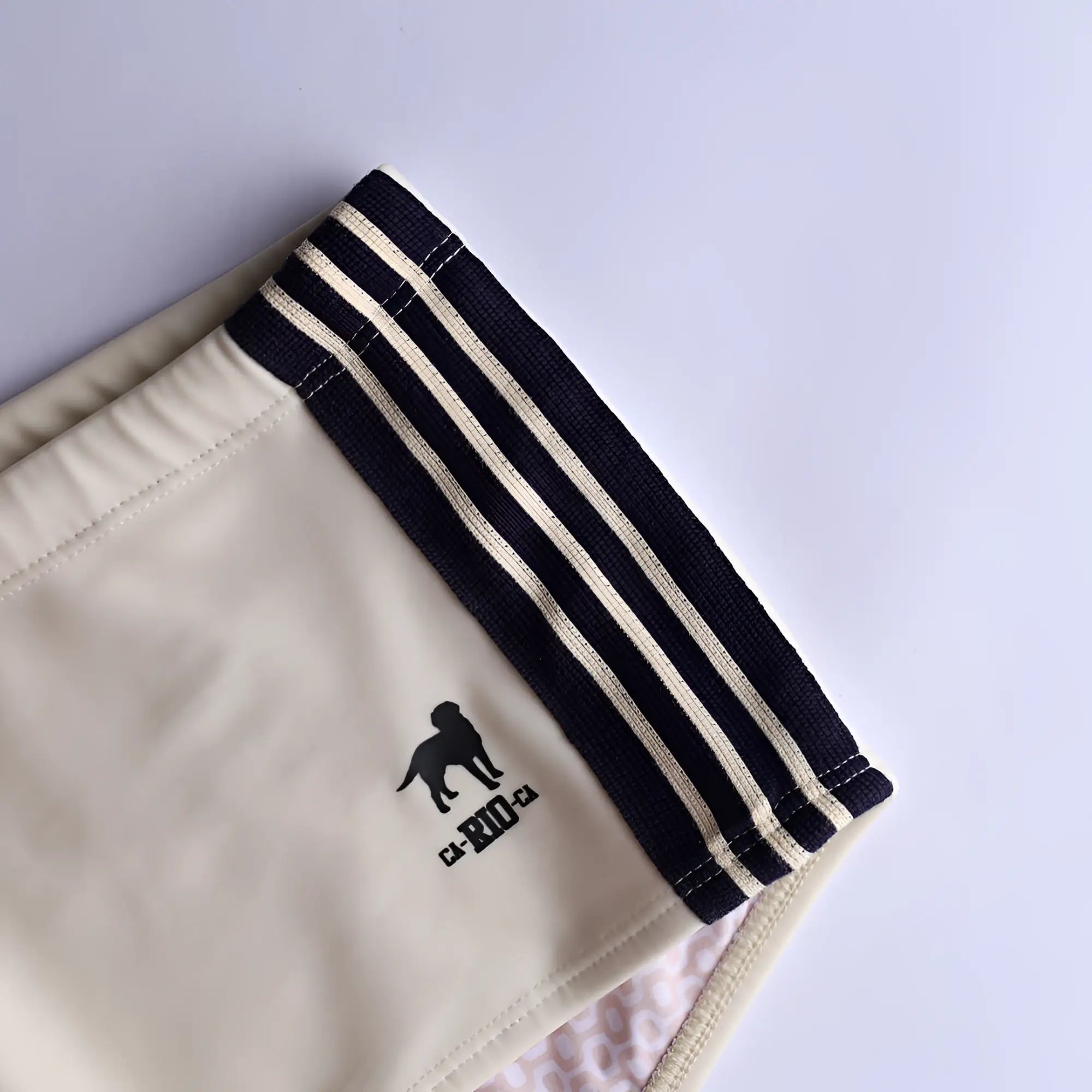 Cream-colored galão creme sunga designer swim shorts with black ribbed waistband white stripes and embroidered dog logo