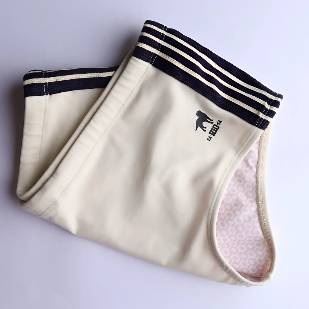 Cream-colored cotton galão creme sunga swim shorts with navy blue striped waistband and black dog logo on front