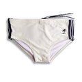 Cream-colored galão creme sunga swim shorts with navy blue side stripes and black dog logo on waistband