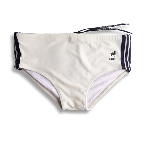 Cream-colored galão creme sunga swim shorts with navy blue side stripes and black dog logo on waistband