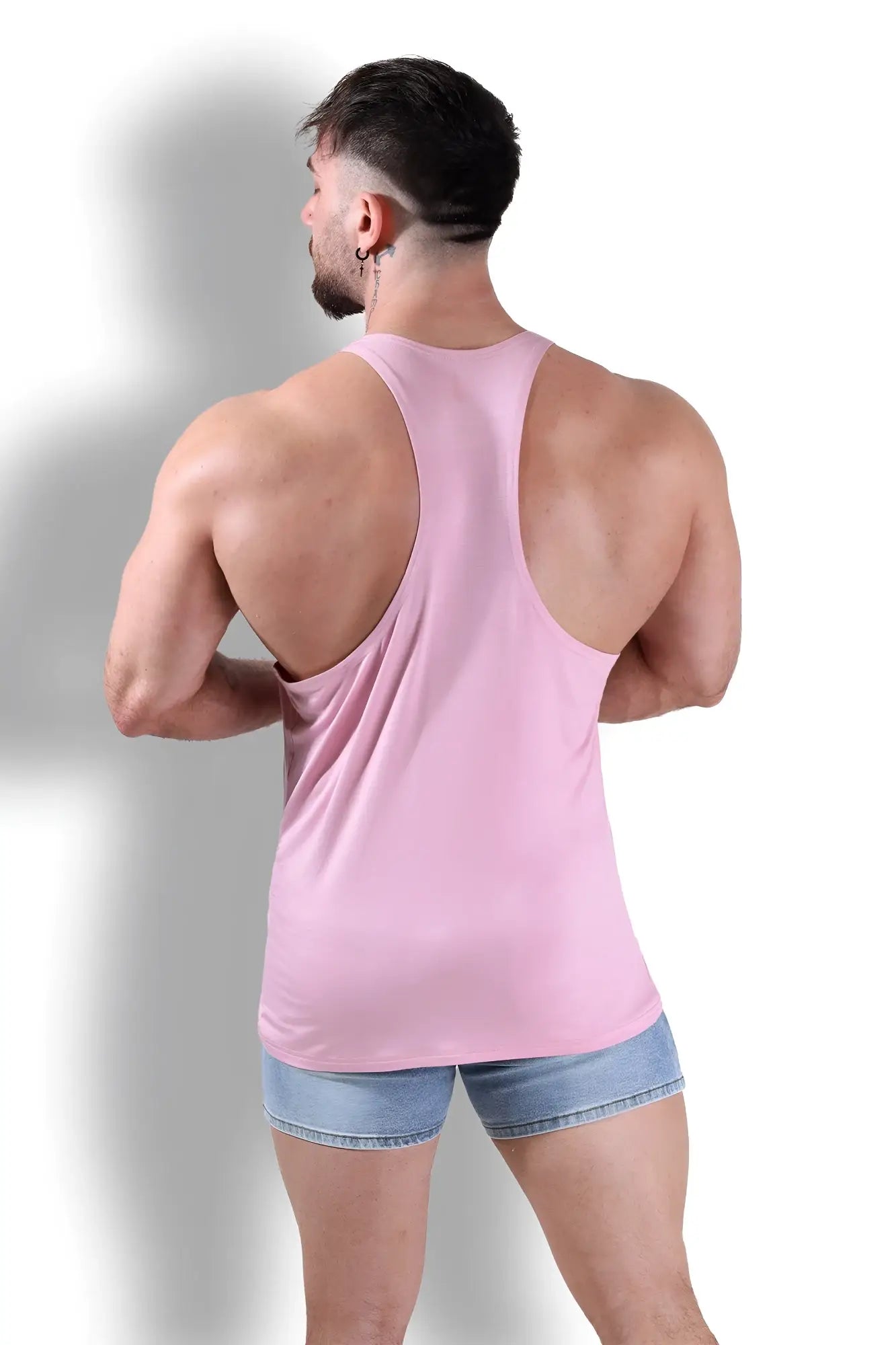 A sleek light pink gym bae classic workout stringer racerback tank top made of smooth stretchy fabric