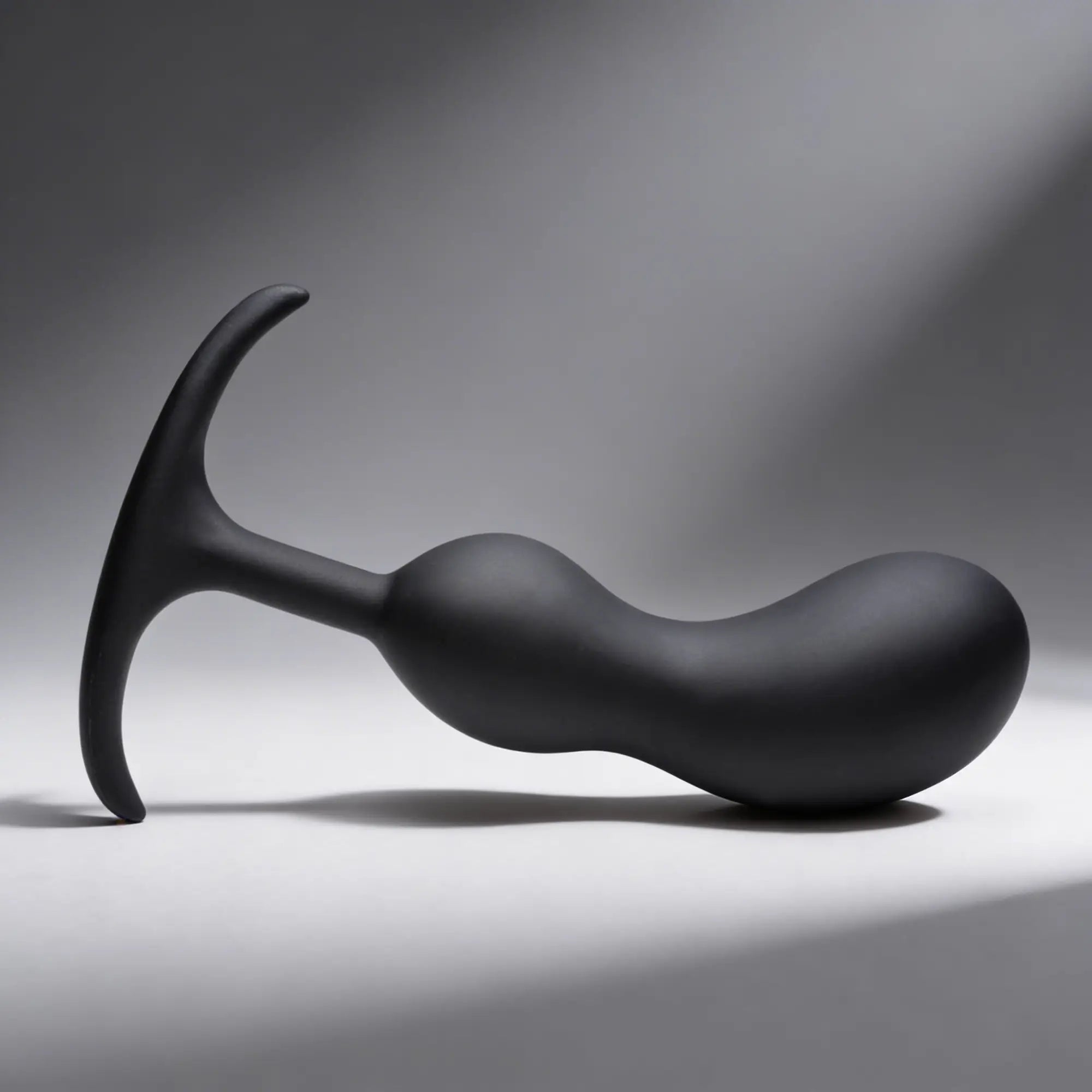 Heavy Hitters matte black silicone prostate plug with a curved, weighted shaft and a flared, ergonomic T-shaped base.