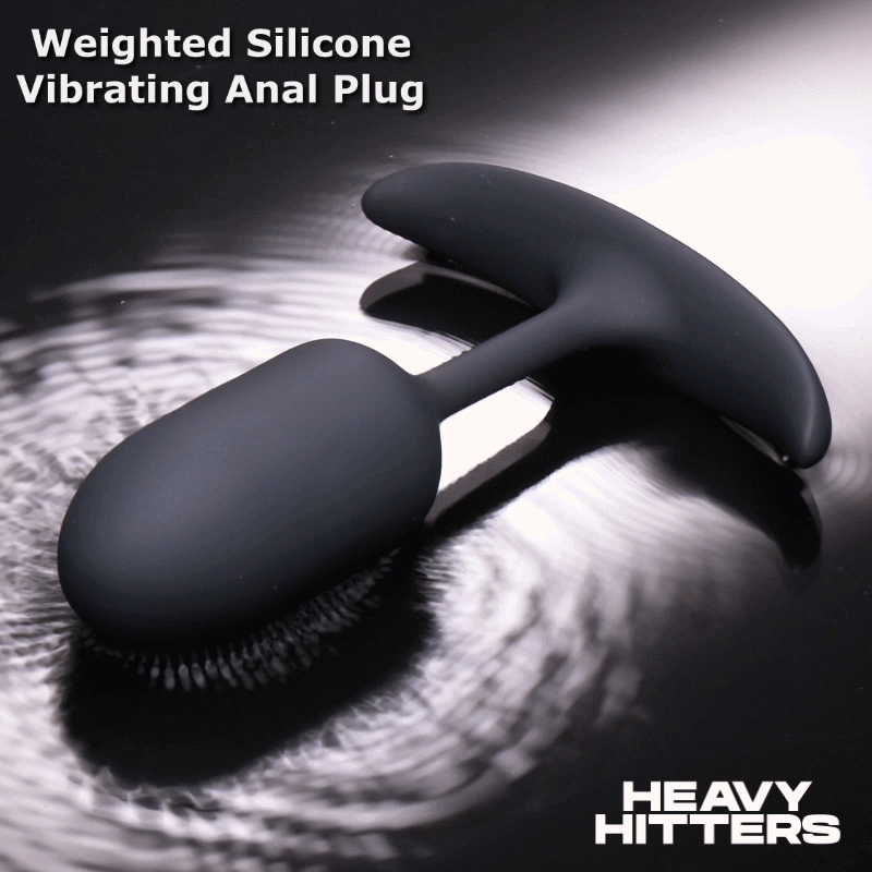 Heavy Hitters matte black silicone vibrating anal plug with a T-shaped base, resting on a rippled water surface.