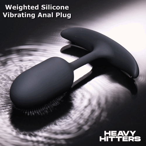 Heavy Hitters matte black silicone vibrating anal plug with a T-shaped base, resting on a rippled water surface.