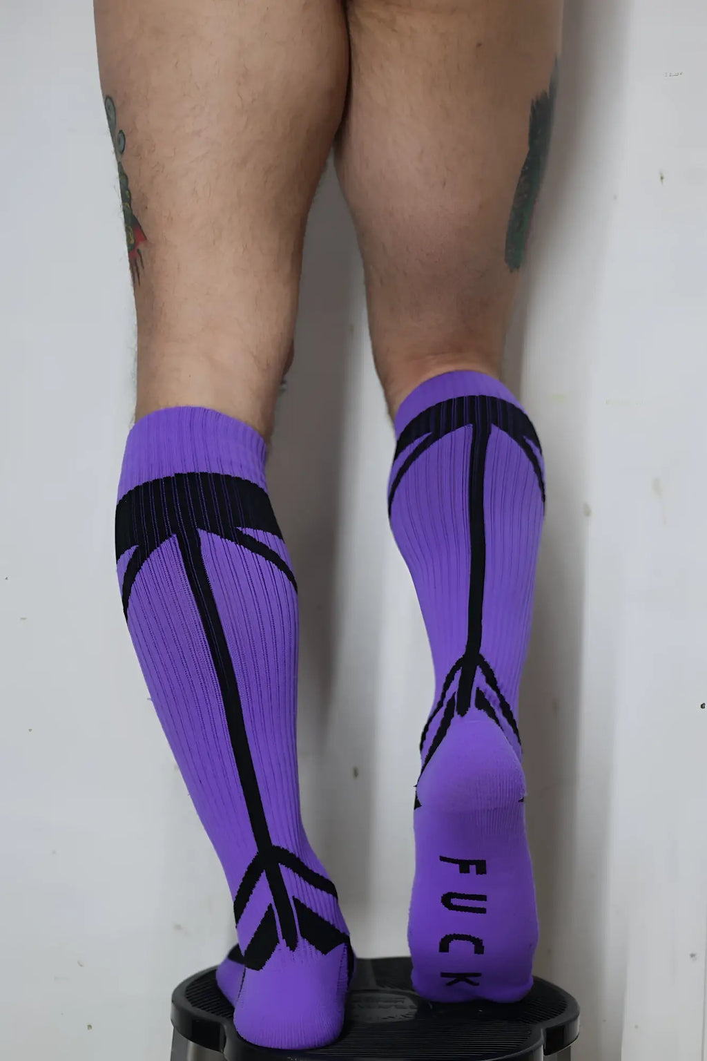 Back view of purple hook up socks featuring black arrow patterns and the word fuck printed on the heel