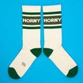 Cream-colored horny crew socks with dark green stripes and toe caps featuring bold white lettering across the band