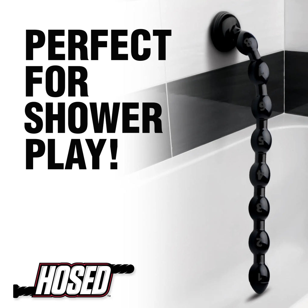 Hosed 19-inch black beaded anal snake suctioned to a white bathroom wall. Text reads: "Perfect for shower play!"