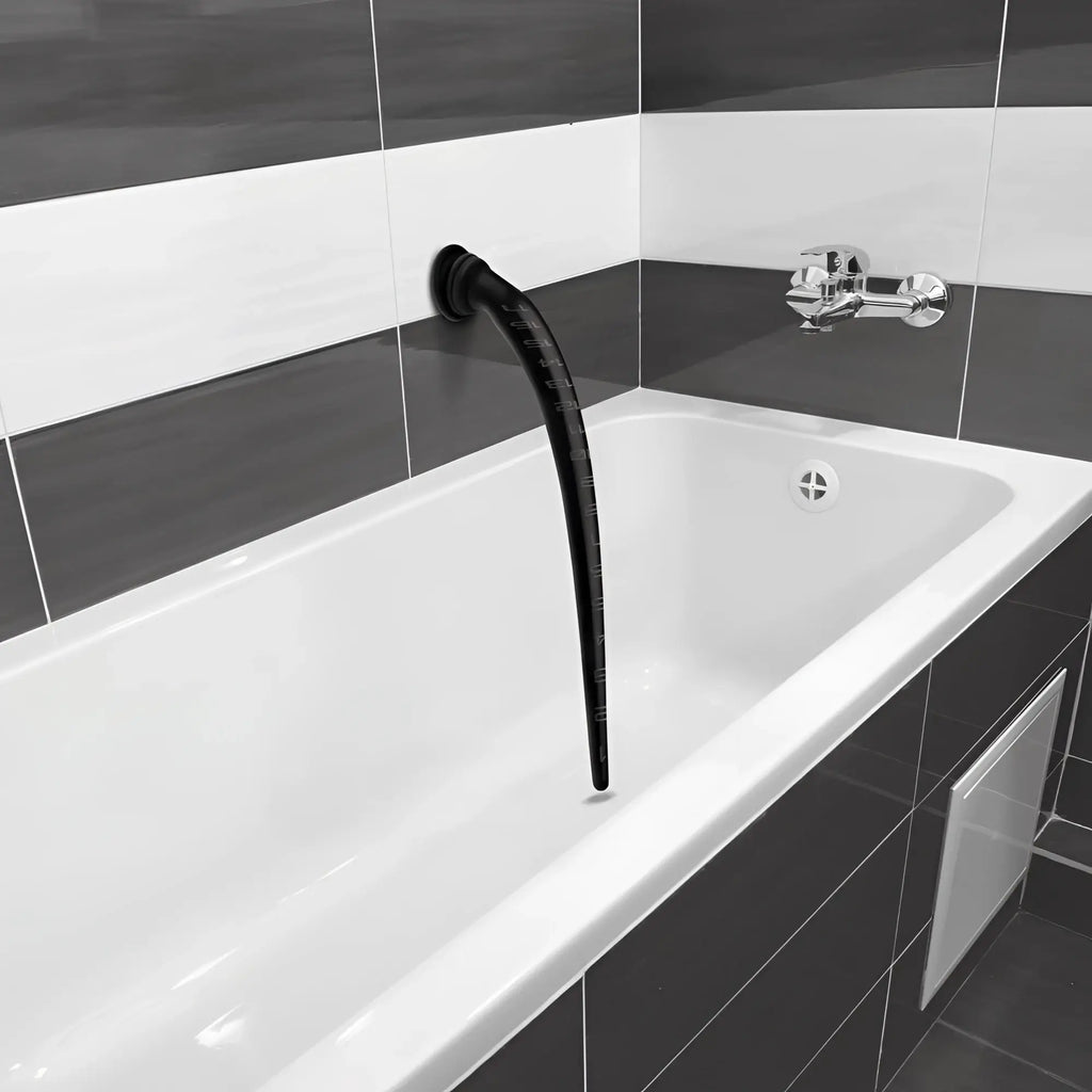 Black, tapered silicone anal hose with depth markings, mounted to a tiled bathroom wall above a white bathtub.