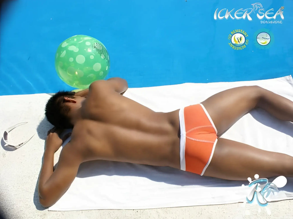 Orange icker sea cheeky mini bikini swimwear with white contrast trim and stitching lying on a towel by the pool