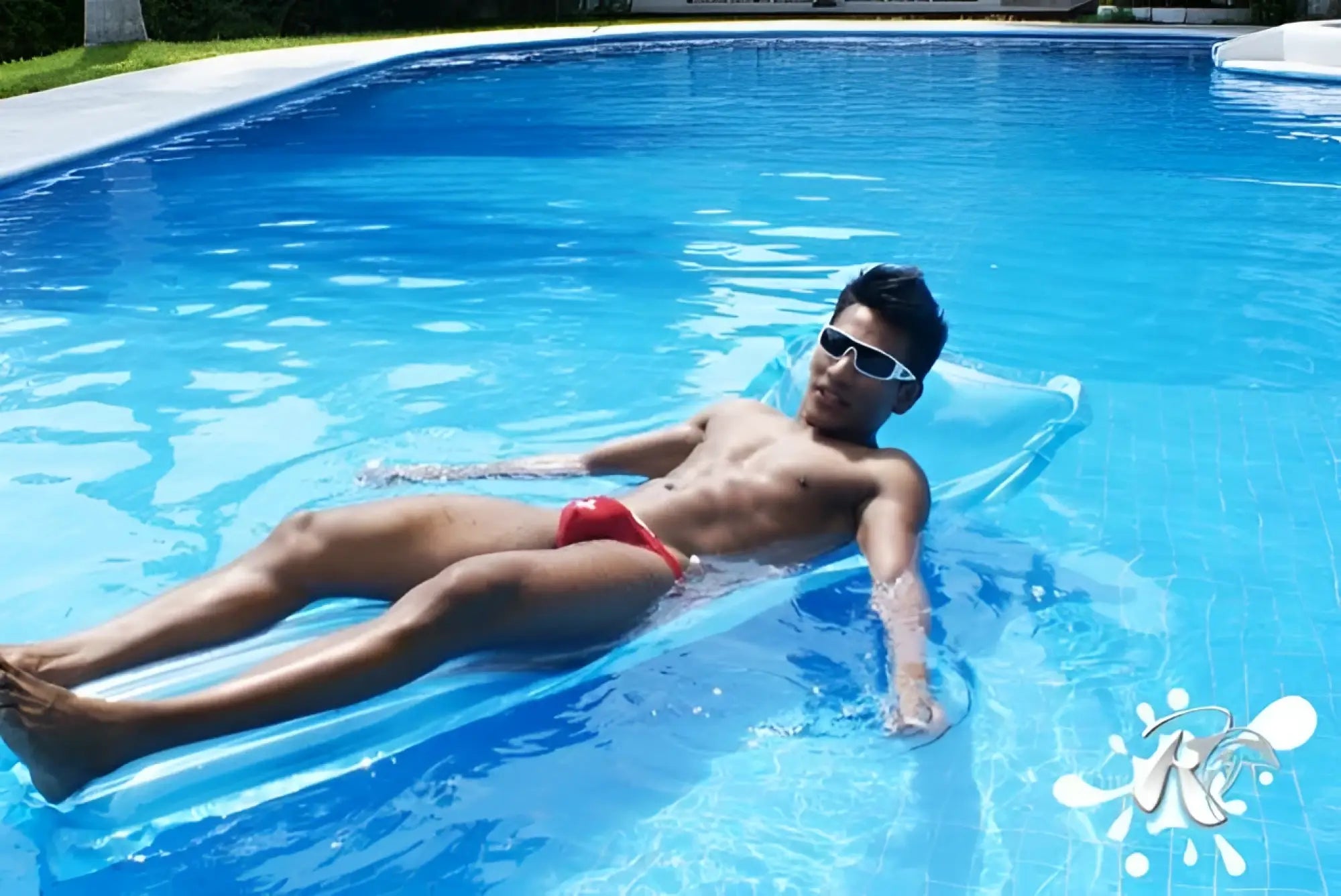 A man wearing icker sea lifeguard micro slip bikini swimwear red floats on a blue inflatable pool float in clear water