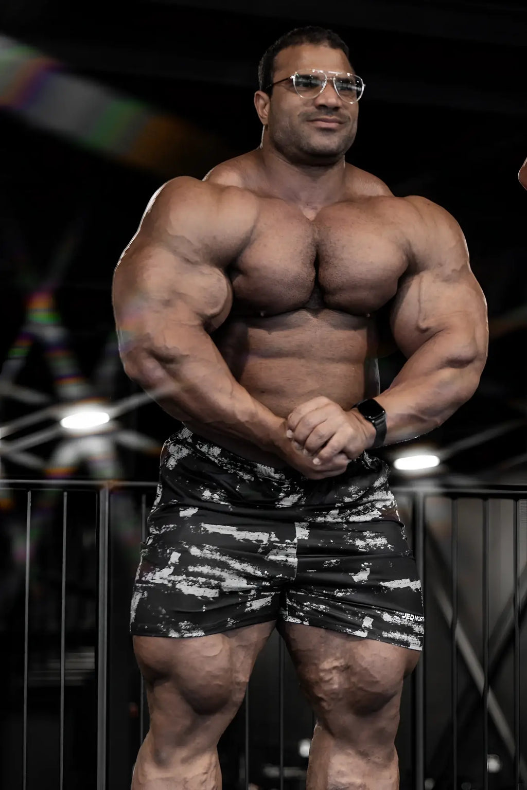 A muscular man wearing agile bodybuilding 4 inch brushed black shorts with white camouflage and zipper pockets