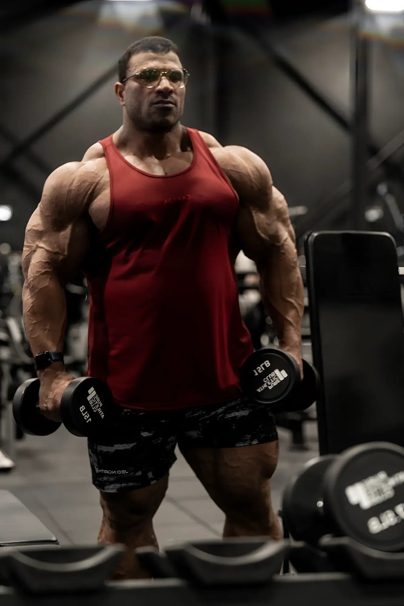 Muscular man wearing agile bodybuilding 4 inch shorts with zipper pockets in brushed black holding dumbbells in gym