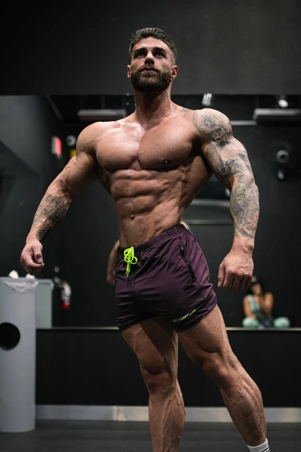 Muscular man wearing jed north agile bodybuilding dark purple 4 inch shorts with neon green drawstring and zipper pockets