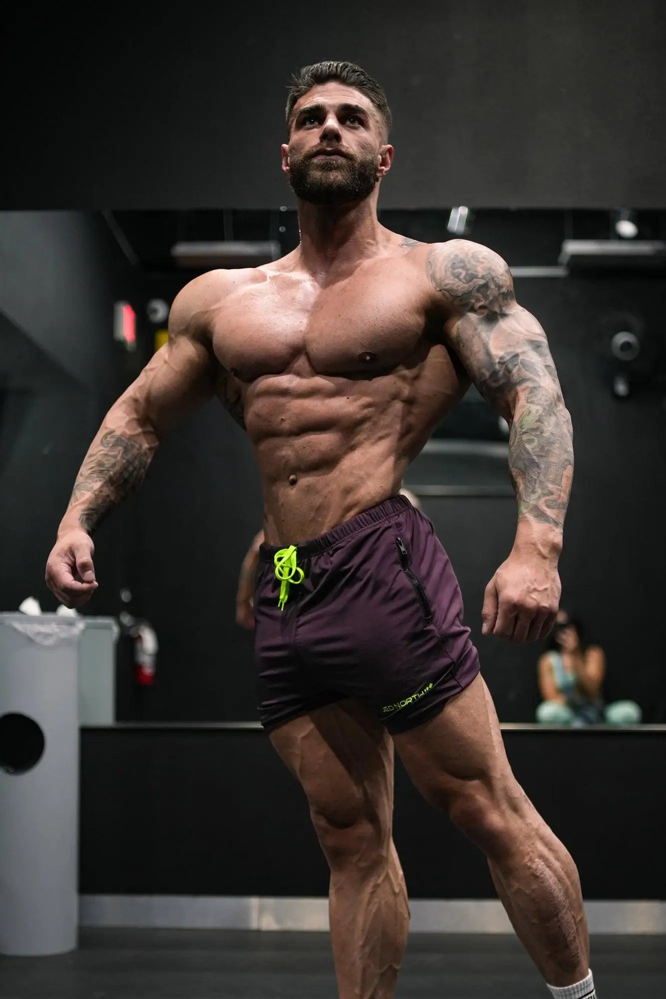 Muscular man wearing jed north agile bodybuilding dark purple 4 inch shorts with neon green drawstring and zipper pockets