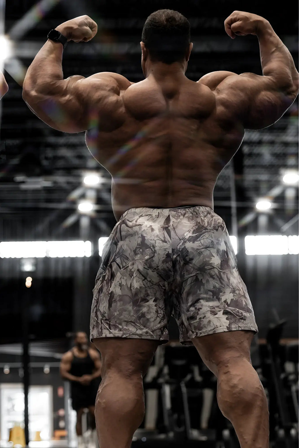 A muscular man wearing agile bodybuilding 4 inch leaf camo shorts with zipper pockets showing front view