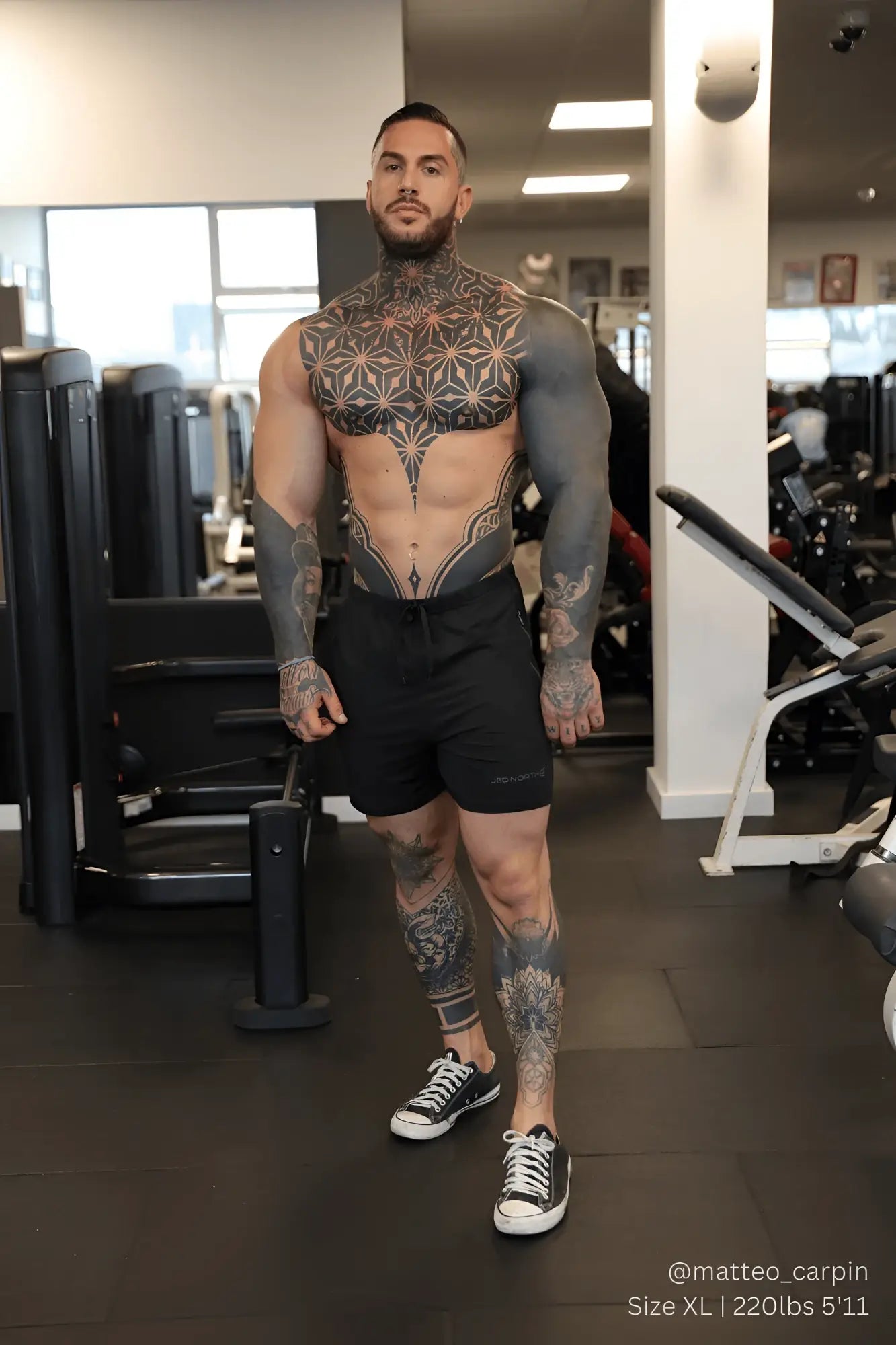 A muscular man with black ink tattoos wearing jed north agile bodybuilding 4 inch noir shorts with zipper pockets in gym